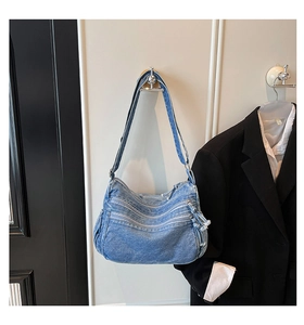 Detail view of light blue denim crossbody bag featuring multiple zipper pockets and strap