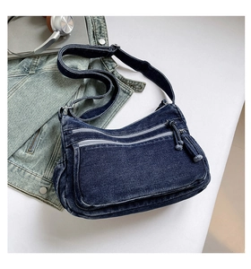 Detailed view of dark blue denim crossbody bag with dual front zipper pockets and fabric pulls
