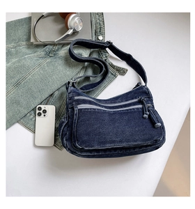 Detail of dark blue denim crossbody bag featuring multiple zippers and adjustable strap