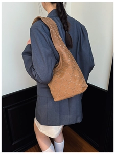 Borsa sottobraccio in camoscio marrone con borchie indossata su blazer grigio