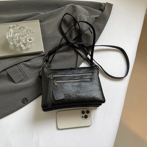 Black multi-pocket crossbody bag in wrinkled leather texture on a minimal grey setting