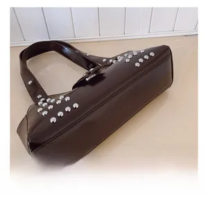 Détail du sac sous l'aisselle marron foncé brillant avec des rivets argentés denses