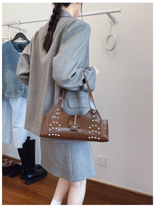 Sac bandoulière marron en cuir glacé avec rivets porté par un mannequin en studio