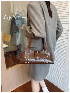 Détail d'un sac porté épaule marron à rivets argentés porté par un mannequin en salle