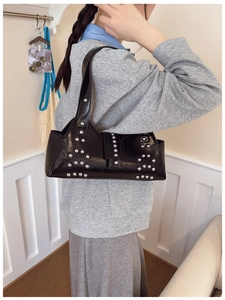 Détail d'un sac à bandoulière en cuir noir avec clous argentés porté par un mannequin