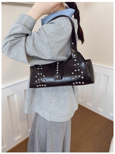 Détail du sac sous le bras en cuir noir brillant avec rivets argentés et lanière