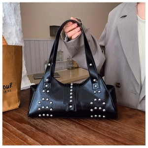 Détail du sac bandoulière en cuir brillant noir avec rivets argentés sur fond urbain