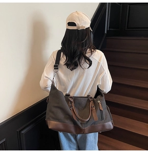 Back view of a large dark grey canvas travel bag with leather trim on a model