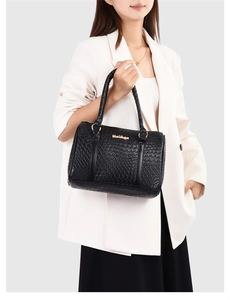 Detail of black PU tote with embossed texture and gold hardware held by a model