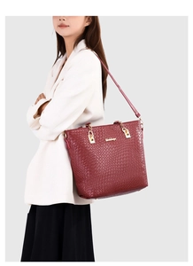 Detail of burgundy tote bag with woven texture, golden chain strap, and logo on shoulder