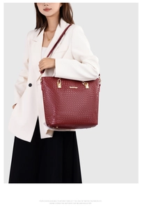 Model wearing a burgundy tote bag with snakeskin embossing and golden chain detail