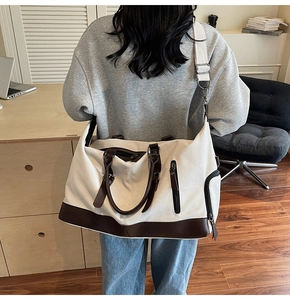 Rear view of a model carrying a large canvas travel bag with leather trim and shoulder strap