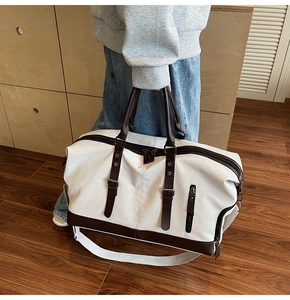 Detail of a large canvas travel bag with brown leather handles and adjustable shoulder strap