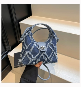 Dettaglio dei bordi in denim sfilacciati e cuciture trapuntate sulla borsa blu scuro