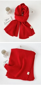 Close-up of thick red knitted scarf with ribbed texture and detailed fabric label