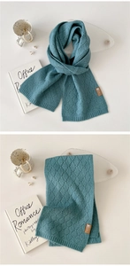 Detail eines blauen Strickschals mit hohlem Rautenmuster und elegantem Lederetikett