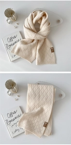 Detail eines cremefarbenen Strickschals mit Rautenmuster und einem edlen Lederetikett