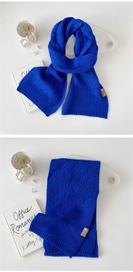 Detail eines klineblauen Strickschals mit Rautenmuster und braunem Lederetikett