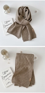 Detail eines dunkel khakifarbenen Strickschals mit Rautenmuster und Lederaufnäher