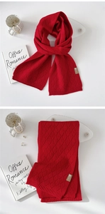 Makrodetail eines roten Strickschals mit Rautenmuster und Logo-Etikett aus Leder