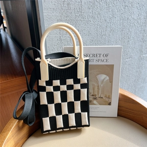 Detail of checkered knit handbag with rigid cream handle and black shoulder strap on chair