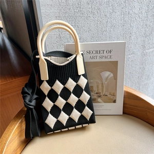 Detail of checkered knit handbag with cream handle and woven shoulder strap on a chair