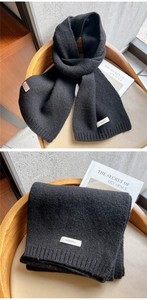 Detail of 100% wool black knitted scarf showing thick ribbed texture and premium material tag