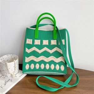 Detail of green knitted mini phone bag featuring white geometric patterns and silicone handle