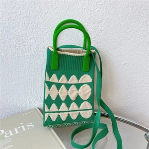 Detail of green knitted mini phone bag with white leaf pattern on a glass surface