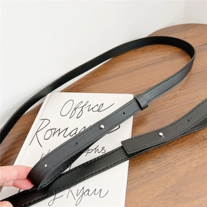 Adjustable black faux leather bag strap with silver metal studs on a minimal wooden desk