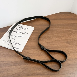 Slim black leather bag strap with silver metal rivets on a dark wood background
