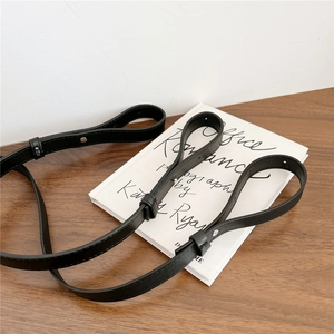 Adjustable black leather bag strap with silver metal buckle on a minimalist desk setup