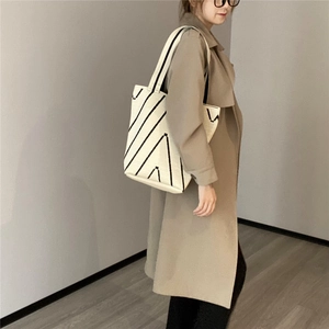 Dettaglio della borsa tote in maglia con motivo a lettera A nera indossata con un trench
