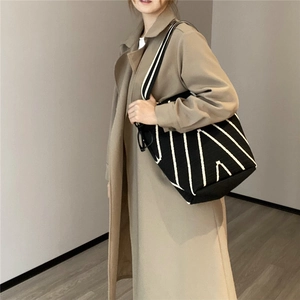 Dettaglio di una borsa tote in maglia a righe geometriche bianche e nere indossata da modella