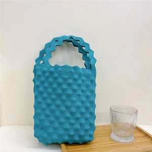 Close-up of blue knitted tote bag with unique wavy textured pattern on a wooden tray