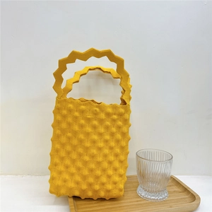 Detailed macro view of yellow bubble knit handbag featuring 3D popcorn texture on a tray