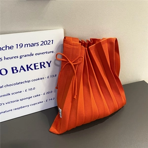Detailed view of an orange pleated knit tote bag with a ribbon tie and woven label