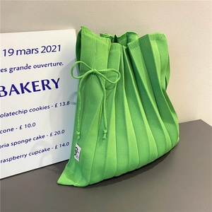 Detail of green knitted tote bag showing pleats, bow drawstring and soft texture