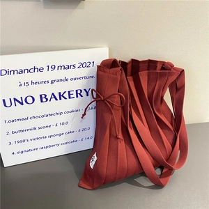Detail of brick red pleated knit tote featuring bow tie accents and fabric texture