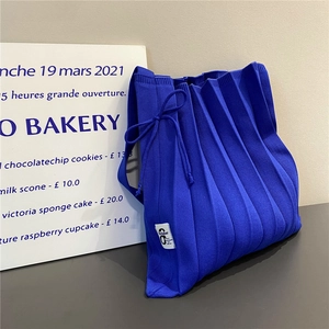 Detail of royal blue pleated knit tote bag featuring a minimalist white woven label