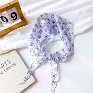 Détail d'un foulard en mousseline lilas à fleurs bleues posé sur un tissu blanc