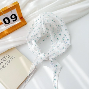 Détail d'un foulard en mousseline blanche avec motifs floraux lilas et bords ourlés