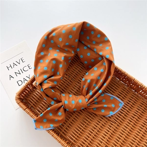 Caramel orange polka dot square scarf with blue edges in a woven basket