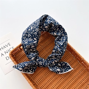 Dettaglio foulard di seta floreale blu navy con motivi crema su vassoio intrecciato