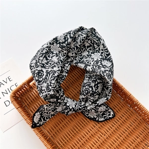 Detailed close-up of a knotted black and white floral cotton linen scarf on a rattan tray