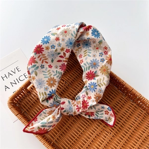 Detail of floral linen small square scarf with red edges on a woven rattan tray
