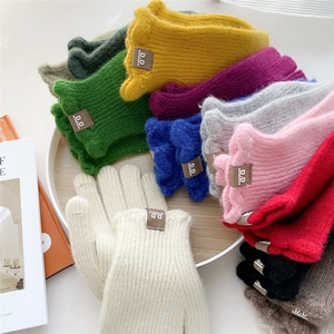 Various colors of winter knitted gloves with ribbed texture and brand label in a tray