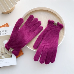 Detail of burgundy knit gloves with ribbed texture and leather logo label on wooden tray