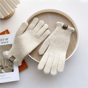 Detail of cream knitted gloves with brown leather tag on a rustic wooden background