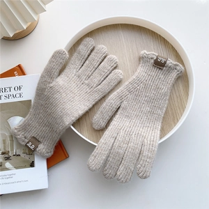 Close-up of oatmeal knitted gloves featuring thick vertical ribbing and brown leather tag